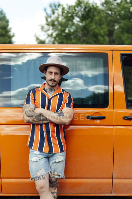 Serious male traveler leaning on van parked in nature and looking at camera during summer adventure — Stock Photo