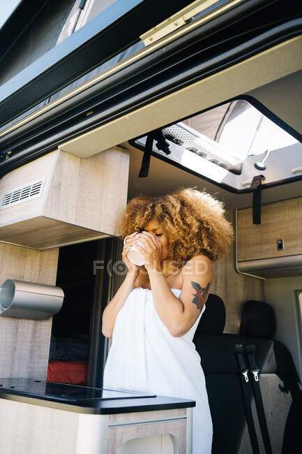 Donna afroamericana rilassata con tazza di bevanda calda e refrigerante all'interno del moderno camper in mattina d'estate — Foto stock