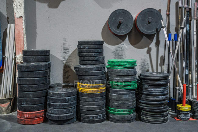 Shabby metal plates for barbell stacked against concrete wall in gym — Stock Photo