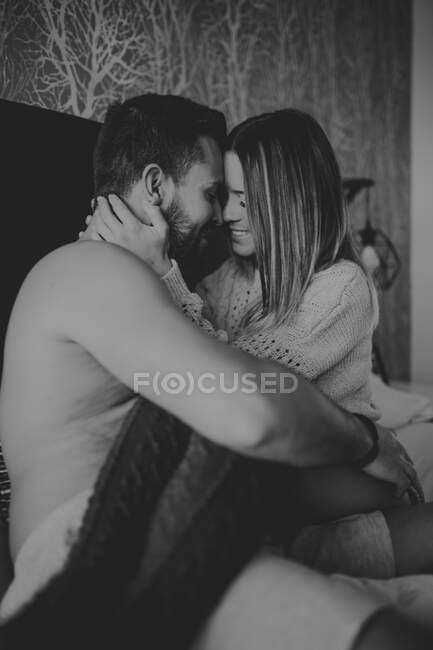 Jovem alegre e mulher sorrindo e abraçando enquanto deitado na cama confortável em casa juntos — Fotografia de Stock