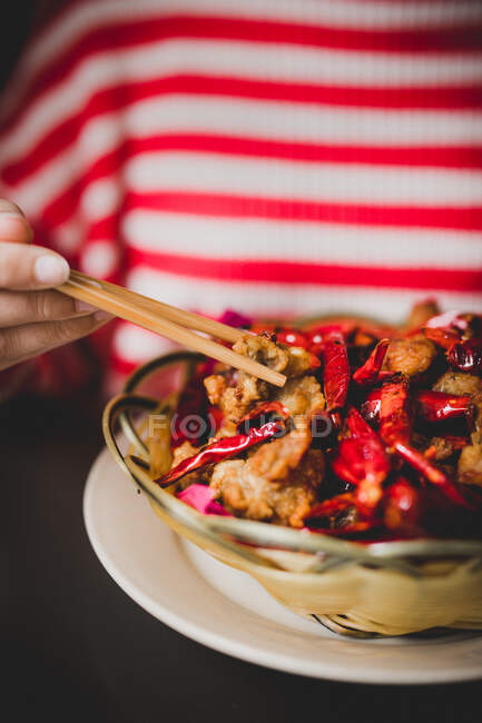 Mano di donna con bacchette mangiare Peperoncini di pollo farina da ciotola di vimini — Foto stock