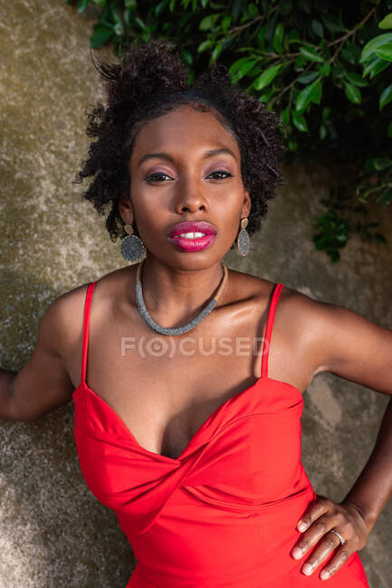 Confident African American female standing with hand on waist and looking at camera near stone wall — Stock Photo