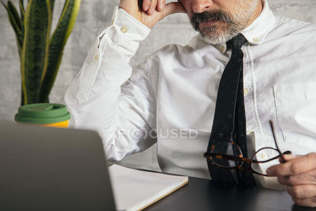 Обрезанный неузнаваемый вдумчивый предприниматель среднего возраста в формальной одежде, работающий на ноутбуке за столом в офисе — стоковое фото