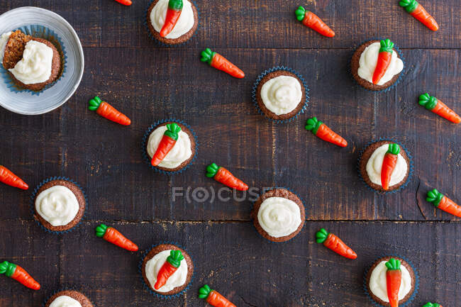 Seamless pattern of composed decorative sweet carrots and cupcakes with cream on wooden background — Stock Photo