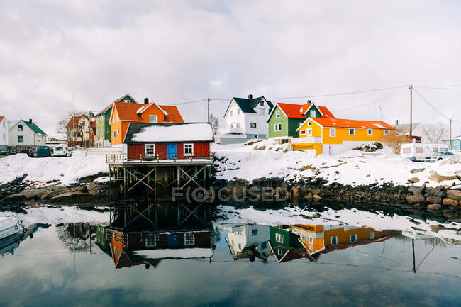 Muelle nevado en pacífico asentamiento costero con casas rojas en día nublado de invierno en las Islas Lofoten, Noruega - foto de stock