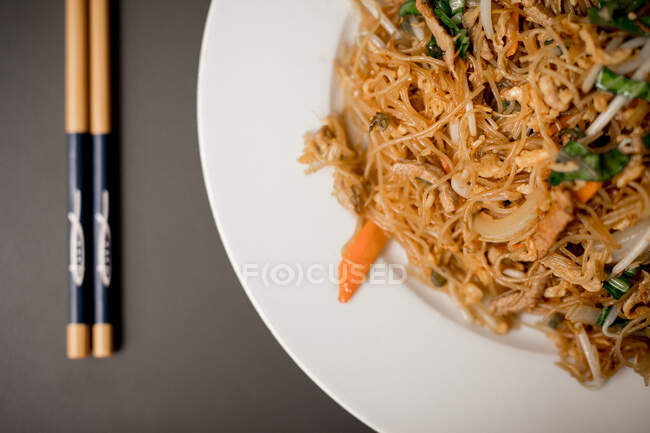 From above composition of plate with beef vegetable noodles and chopsticks placed on grey table — Stock Photo