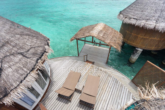 Dall'alto di ville sull'acqua con sedie a sdraio bungalow in legno vicino all'oceano alle Maldive nella giornata di sole — Foto stock