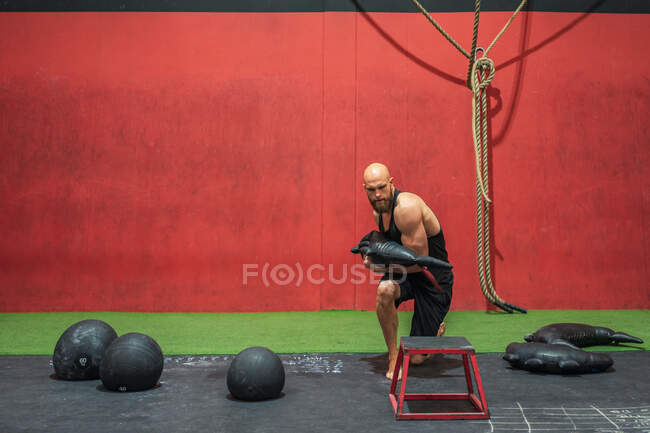 Sportif puissant avec sac lourd marchant et poussant sur les tabourets pendant l'entraînement fonctionnel dans la salle de gym moderne — Photo de stock