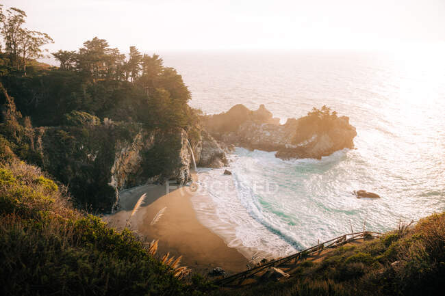 High angle of wonderful scenery of stormy ocean water with foam waves washing sand beach against foggy highland shoreline under gray sky in Big Sur — Stock Photo