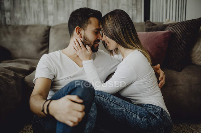Lächelnde Frau umarmt und küsst fröhlichen Mann auf die Stirn, während er auf dem Boden sitzt — Stockfoto