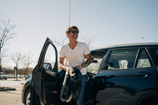 Allegro autista maschile in occhiali da sole uscire dalla macchina moderna mentre distoglie lo sguardo nella giornata di sole — Foto stock