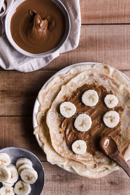 Top view of pieces of fresh banana on palatable crepes with nut butter on timber table — Stock Photo
