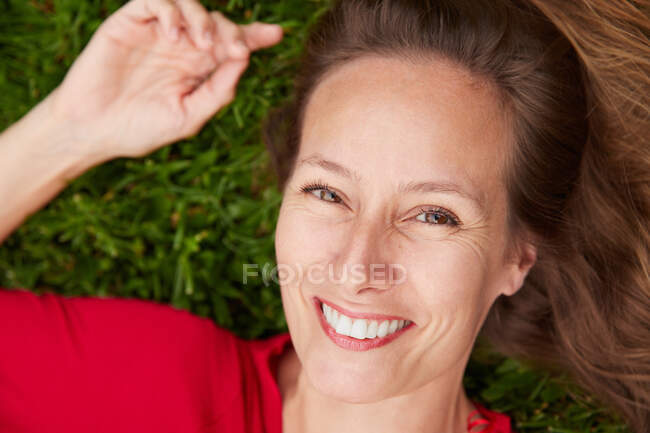 Mulher vestida de vermelho deitada no chão em um parque com grama e olhando para a câmera — Fotografia de Stock