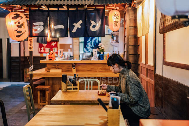 Jeune femme asiatique en pull manger au comptoir en bois dans le café — Photo de stock