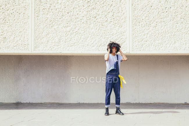 Sonriente joven étnico masculino en desgaste retro tocando el pelo rizado mientras mira la cámara en el pavimento - foto de stock