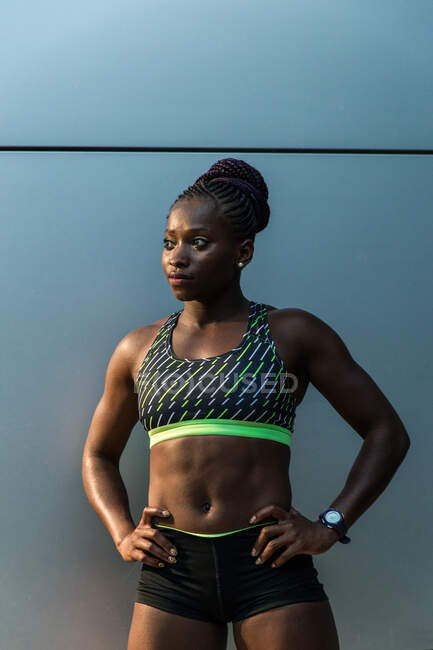 Femme noire positive en tenue de sport gardant les bras dans un bocal et regardant loin tout en se tenant debout sur un fond flou de la rue de la ville — Photo de stock