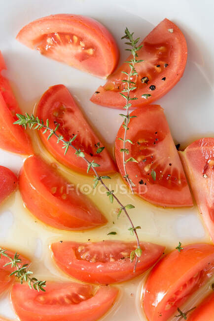 Vista superior de apetitosas piezas de tomate con hierbas verdes servidas en el plato sobre la mesa - foto de stock