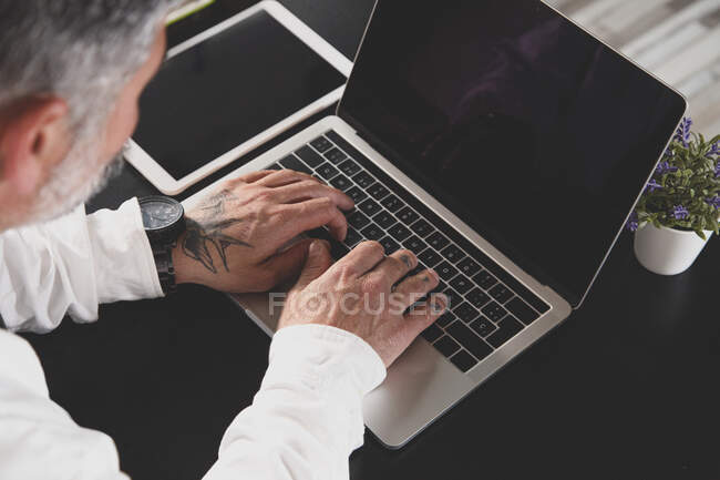 Сверху обрезается неузнаваемый предприниматель среднего возраста в формальной одежде, работающий на ноутбуке за столом в офисе — стоковое фото