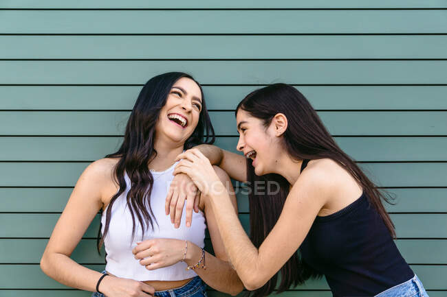 Positive female teen leaning on shoulder of sibling while having fun on green background in daytime — Stock Photo