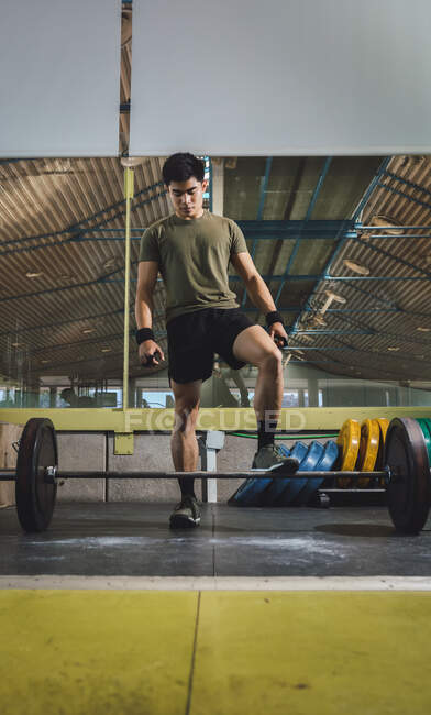 Сфокусований азіатський спортсмен робить мертву ходу з важким ударом під час тренувань у спортзалі, дивлячись на камеру — стокове фото
