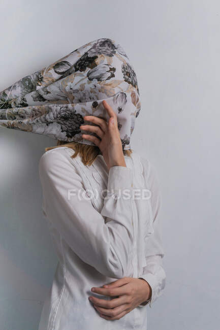 Anonymous female in white blouse with silk scarf with floral print on face standing against white wall — Stock Photo
