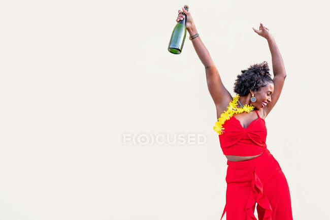 Deliziosa donna afroamericana in collana di fiori indossando luminoso in piedi generale con bottiglia di champagne sullo sfondo bianco — Foto stock