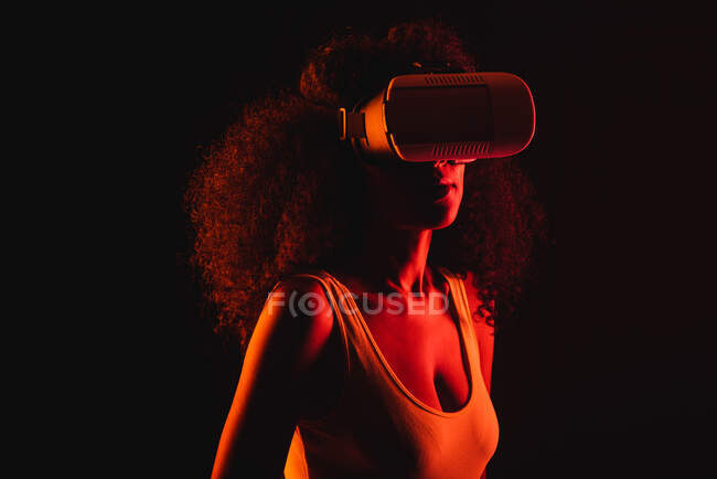 Mujer étnica anónima explorando la realidad virtual en auriculares sobre fondo negro - foto de stock