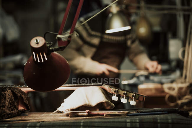 Vista laterale di anonimo artigiano maschio utilizzando macinazione pietra mentre levigatura piccolo dettaglio in legno della chitarra al banco da lavoro — Foto stock
