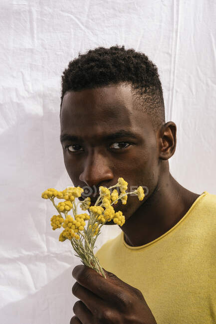 Homme afro-américain avec bouquet de fleurs sauvages jaunes regardant la caméra sur fond blanc — Photo de stock