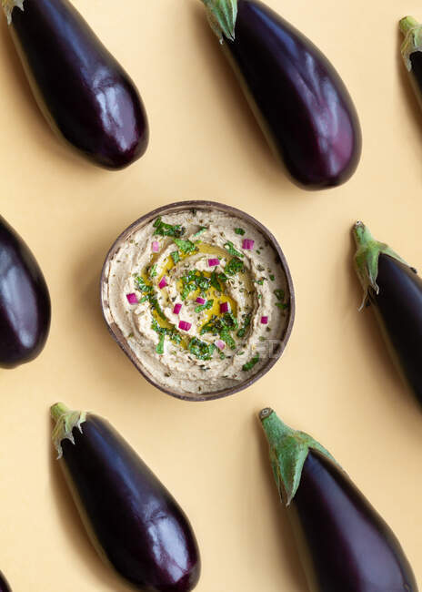 Top view of fresh ripe aubergines placed on beige table with bowl of appetizing traditional Baba ghanoush dish — Stock Photo