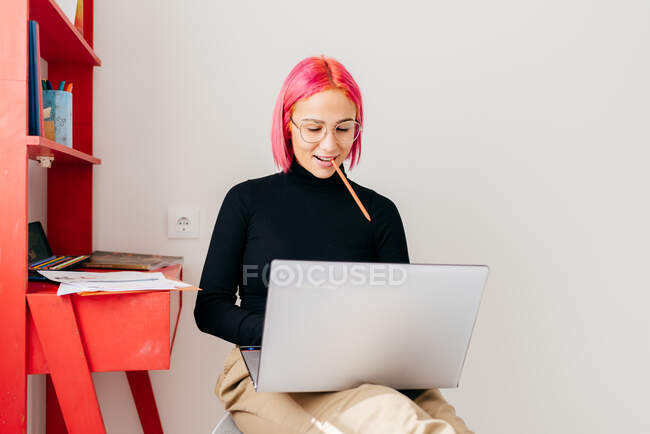 Focused young female freelancer in casual clothes sitting on chair and using laptop while working on project in light modern apartment — Stock Photo