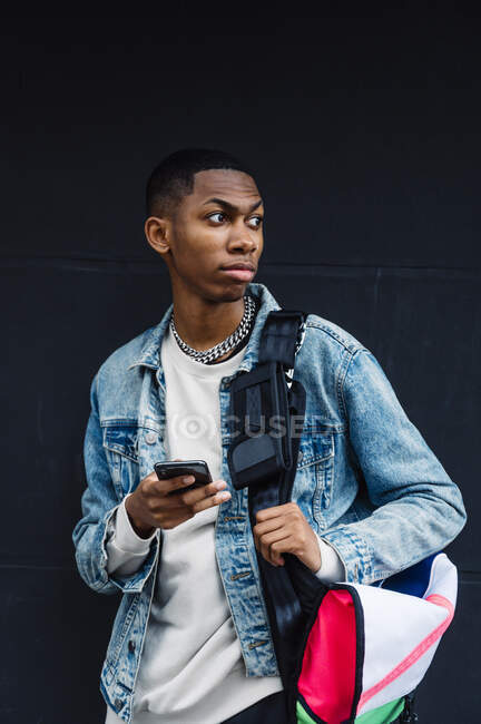 Jovem negro com celular e mochila na rua — Fotografia de Stock