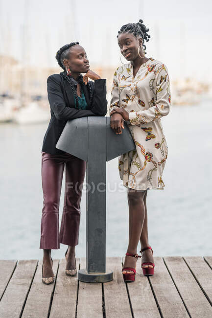 Moda de moda sonriente damas afroamericanas pasar tiempo juntos y hablar juntos en el parque en un día brillante - foto de stock
