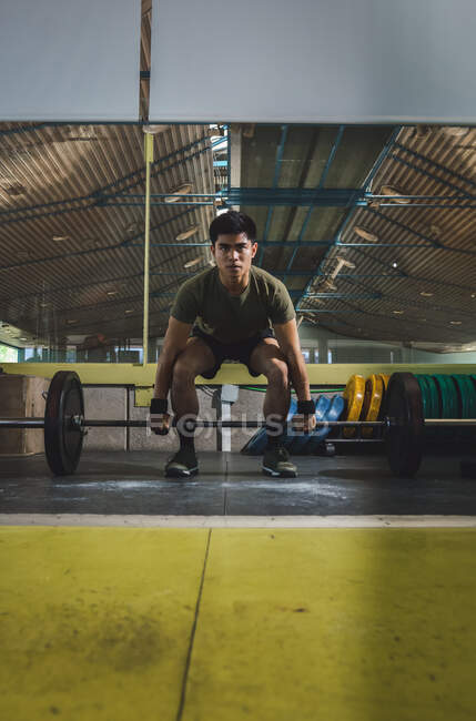 Focalisé asiatique athlète masculin faisant haltérophilie avec haltère lourd pendant l'entraînement dans la salle de gym détournant les yeux — Photo de stock