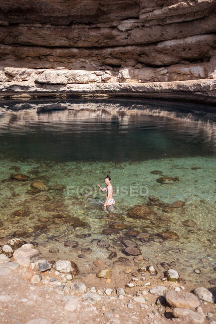 Relaxed asian woman looking back to camera on transparent water of Bimmah Sinkhole surrounded by rough rocks during travel in Oman — Stock Photo
