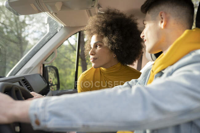 Чорна жінка дивиться далеко, сидячи на пасажирському сидінні автомобіля біля водія чоловічої статі під час дорожньої поїздки в сільській місцевості — стокове фото