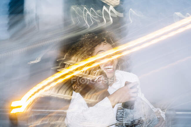 Неузнаваемый веселый черный парень в стильном наряде, катающийся на спине к счастливой девушке, делая селфи на мобильном телефоне возле замораживающих огней на улице — стоковое фото