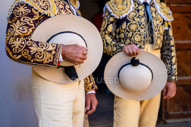 Cultivar toreros irreconocibles en traje tradicional decorado con bordados sosteniendo sombreros y preparándose para el festival corrida - foto de stock
