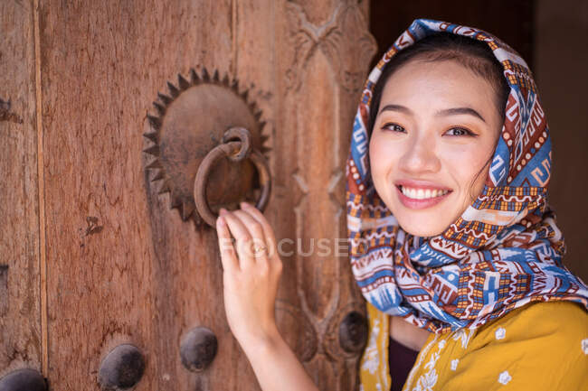 Азиатка с платком рядом со старой деревянной дверью — стоковое фото