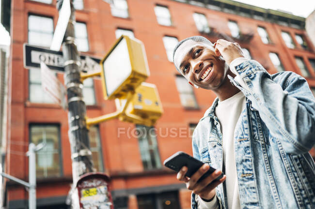 D'en bas contenu gai Afro-Américain gars en denim veste à la mode surf téléphone mobile moderne pendant la promenade en ville — Photo de stock