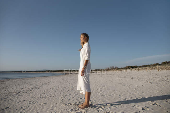 Donna bionda dai capelli lunghi in piedi sulla spiaggia guardando in lontananza — Foto stock