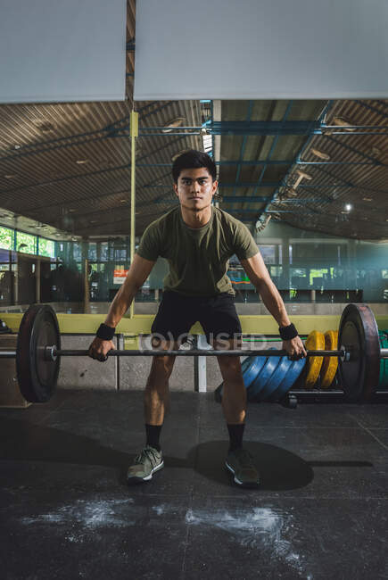 Focalizzato asiatico atleta maschio facendo stacco con pesante bilanciere durante l'allenamento in palestra guardando altrove — Foto stock