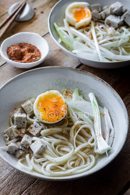 Frische und gekochte Ramen-Nudeln mit Tofu, Eiern und Gemüse, serviert auf einer Keramikschale auf einem Holztisch — Stockfoto
