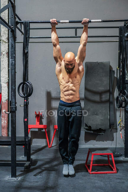 Full body shirtless bearded sportsman hanging on bar and doing pull ups during intense training in contemporary gym — Stock Photo