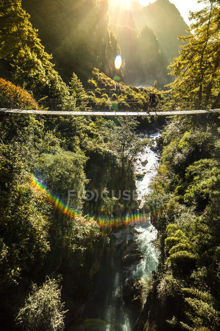 Unrecognizable explorer walking along metal suspension footbridge over fast river in Himalayas mountain range in Nepal — Stock Photo