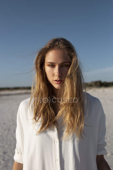 Femme blonde aux cheveux longs debout sur la plage regardant la caméra — Photo de stock