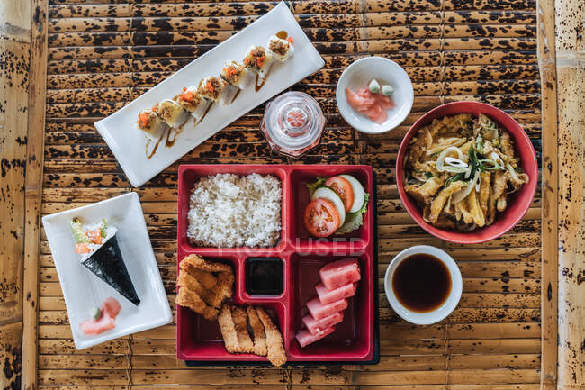 Вид на вкусную еду из суши-роллов и шишек с куриными полосками во фритюре и приготовленным рисом на коврике — стоковое фото