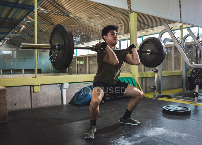 Focalisé asiatique athlète masculin faisant haltérophilie avec haltère lourde pendant l'entraînement dans la salle de gym — Photo de stock
