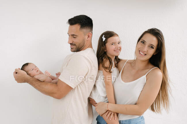 Encantado casal com bebê nu e linda menina de pé no fundo branco — Fotografia de Stock