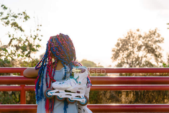 Back view of anonymous Mexican kid with colorful braids admiring trees while leaning on fence in evening — Stock Photo
